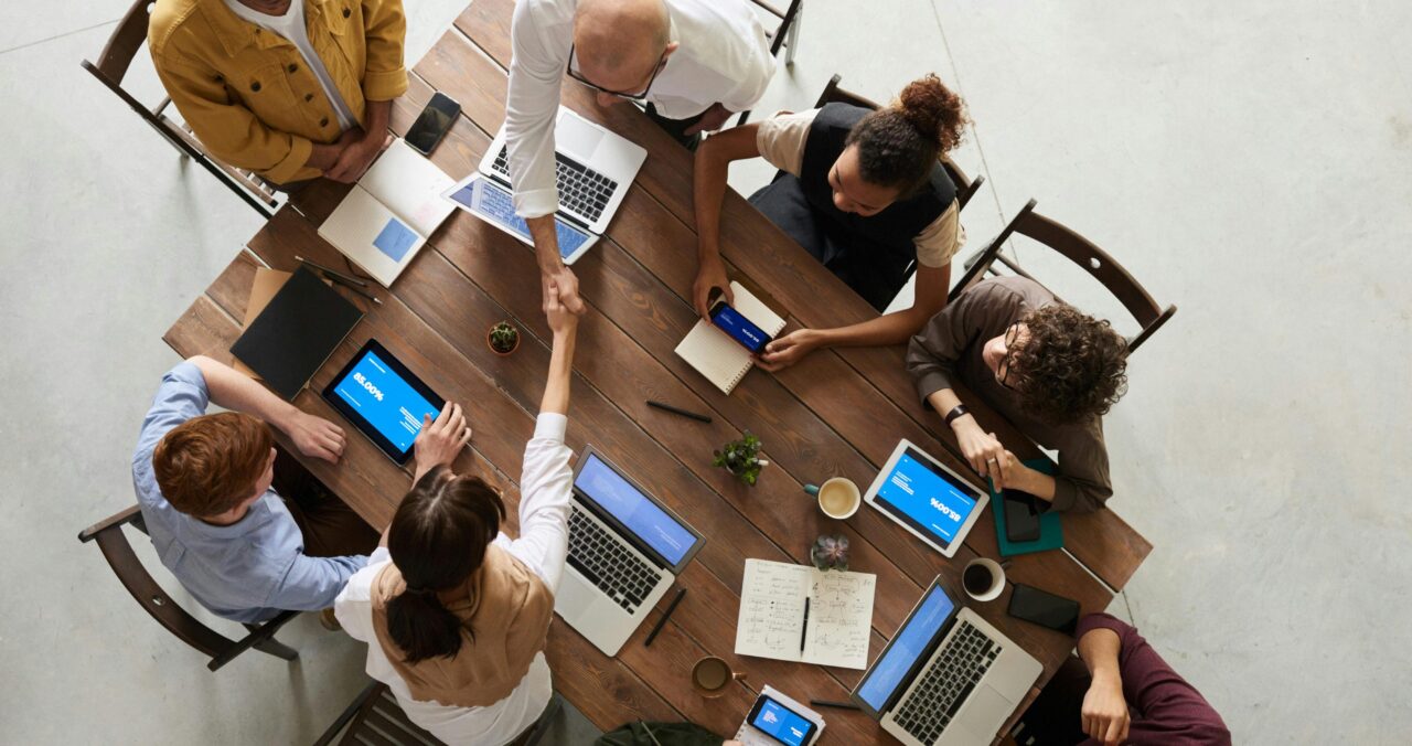 A birds-eye view of a group of people sitting at a wooden table shaking hands.