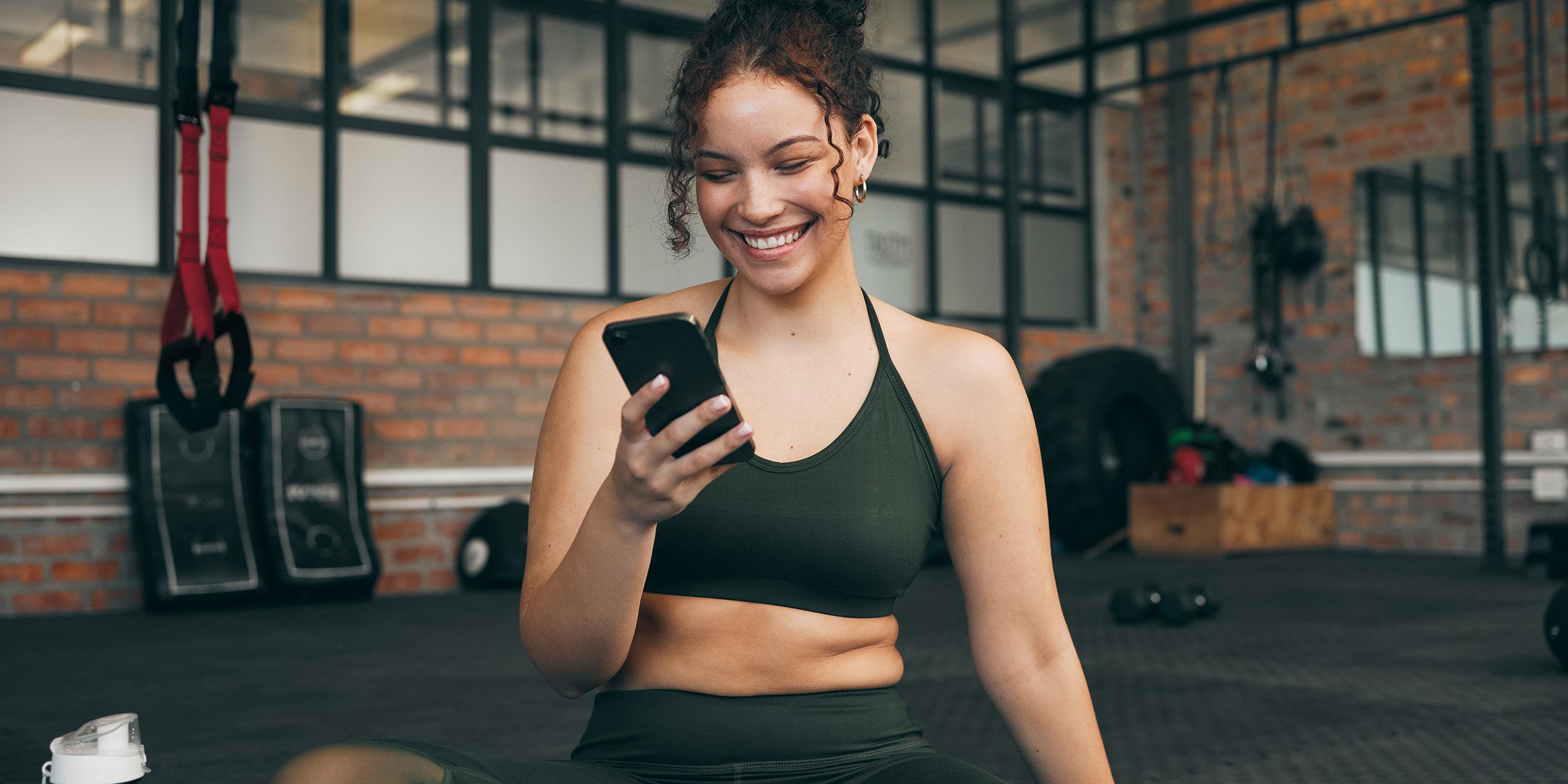 Happy woman, fitness and phone at gym for a workout, training and body wellness with a mobile app. .