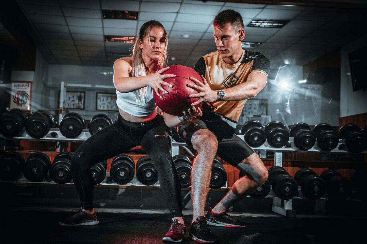 A man and a woman working out in a gym sharing weights.